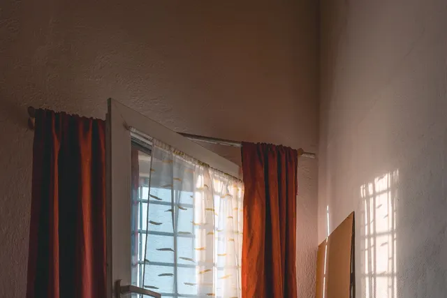 Red curtain panels and a sheer voile hung on a rod across a sunlit window.