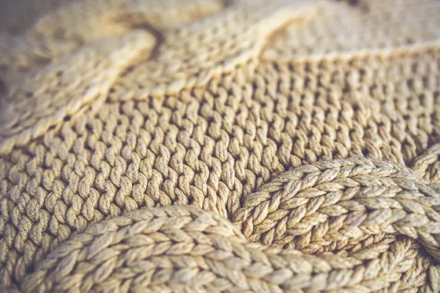 A close-up of a chunky cable-knit throw in warm beige.