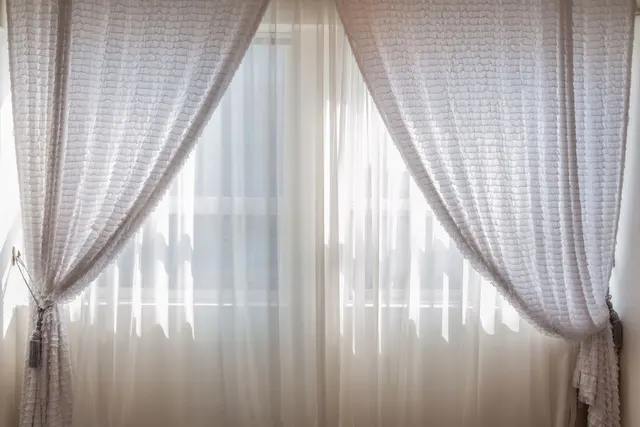 A washed curtain panel hanging back on its rod while still damp, the hem clear of the floor and the fabric falling in even folds.