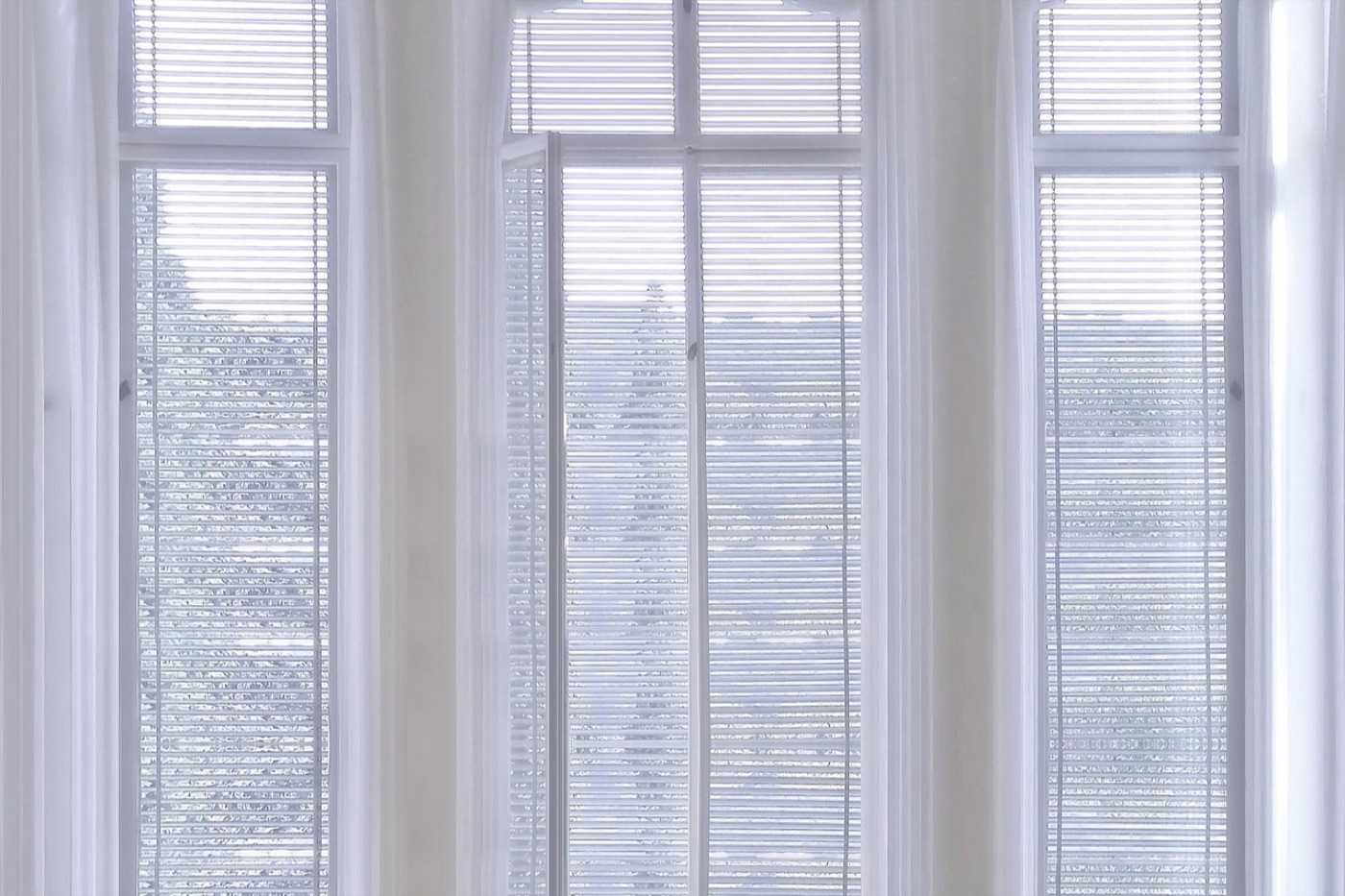 A curved ceiling-mounted curtain track following the angles of a three-facet bay window with light linen curtains.