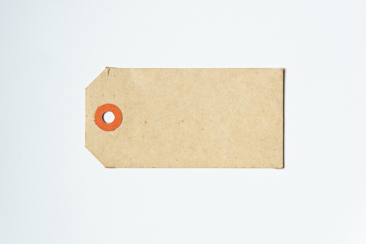 A plain blank paper tag with a reinforced eyelet, the kind sewn into a rug or textile product before the specification is printed on it.