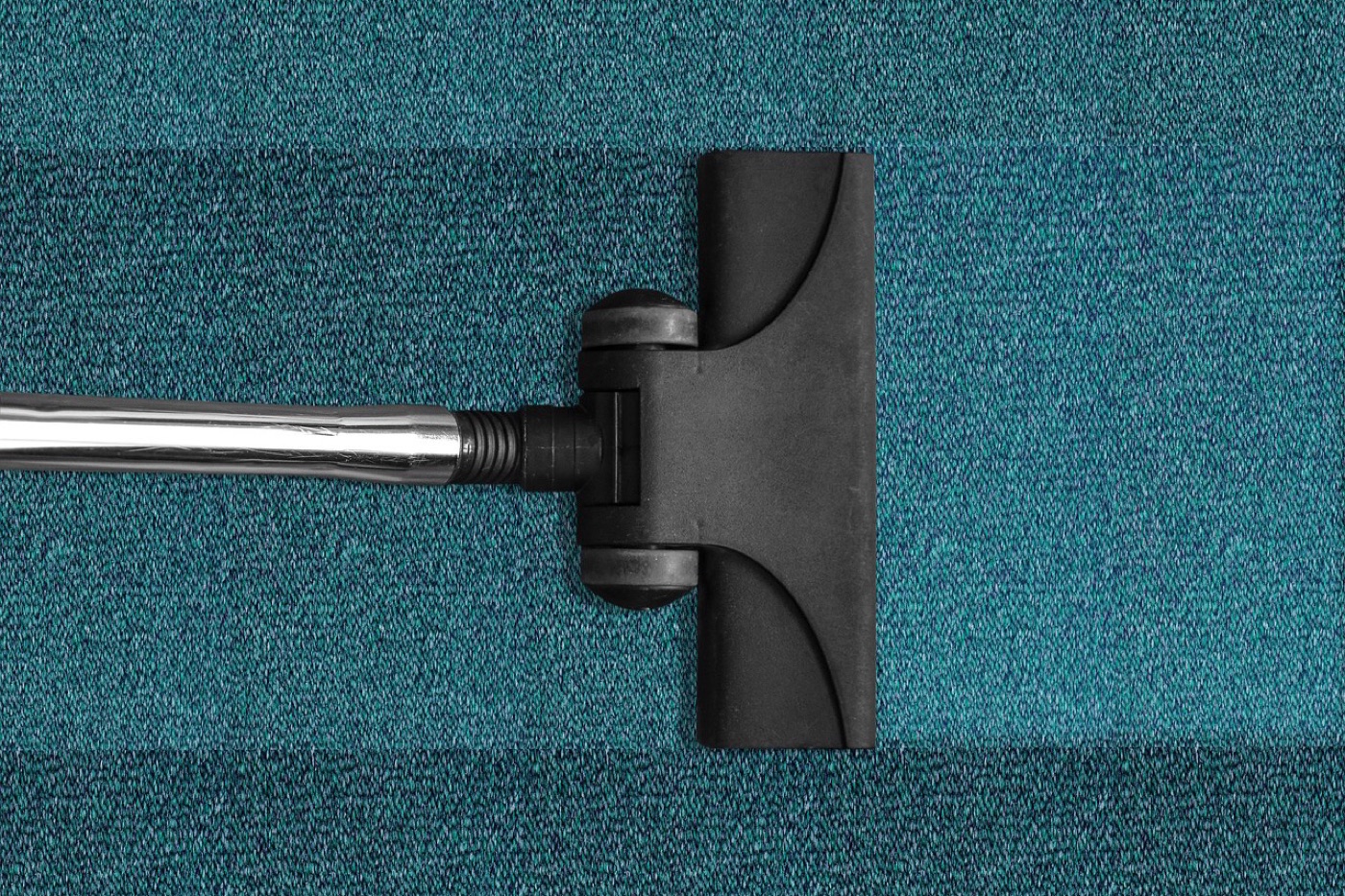 A vacuum cleaner head moving across a medium-pile grey rug in a living room.