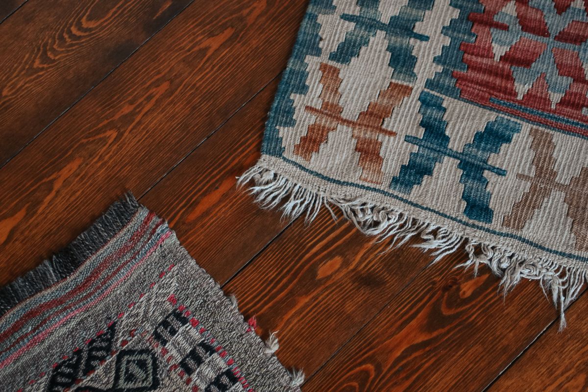 The underside of a machine-made area rug turned back at the corner, showing the cream latex backing and the woven secondary sheet beneath it.