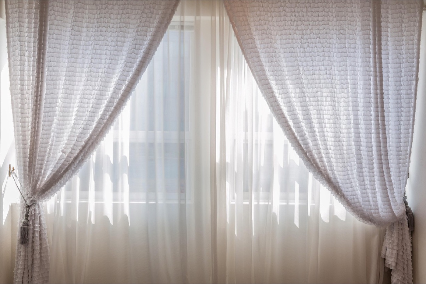 White sheer curtains diffusing bright daylight across a window seat in a plain room.