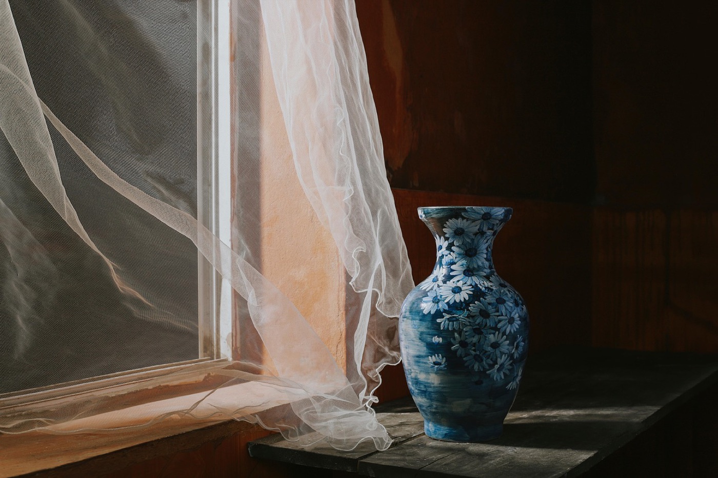 A pale curtain panel by a bright window with its fold edges visibly lighter than the protected inner folds.