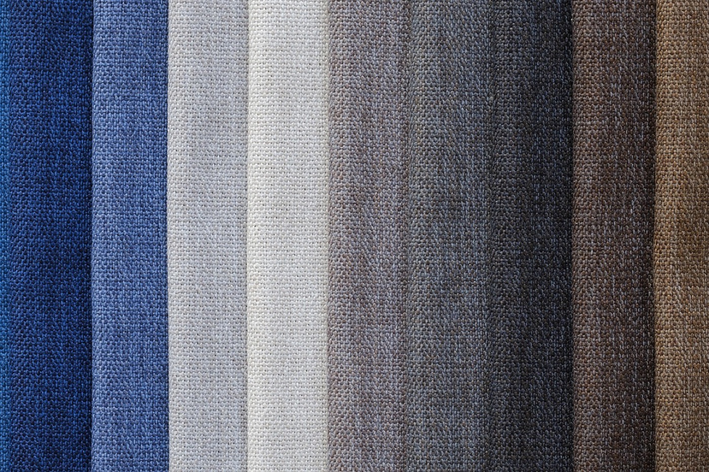 Several fabric swatches spread across a wooden table beside a window, lit by daylight from the left.