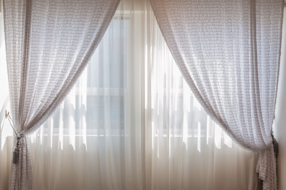 A washed curtain panel hanging back on its rod while still damp, the hem clear of the floor and the fabric falling in even folds.