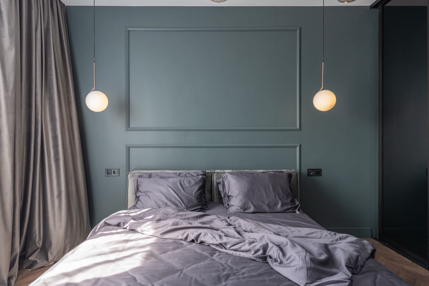 A made-up bed with two grey pillows resting against a dark green headboard wall.